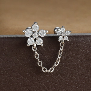 Détail macro de boucles d'oreilles double piercing en acier avec fleurs et chaîne