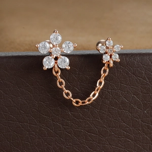 Détail macro de boucles d'oreilles fleurs en or rose avec zircons et chaîne de liaison