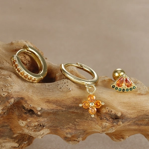 Detailed close-up of a three-piece gold earring set with orange zircon and watermelon studs