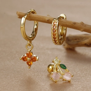 Macro detail of gold clover zircon earrings and cherry stud with gemstone inlays