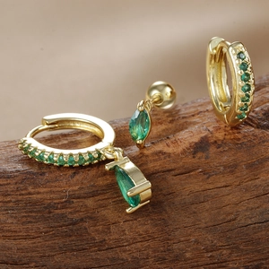 Primer plano de pendientes de aro dorados con gotas de circón verde sobre madera