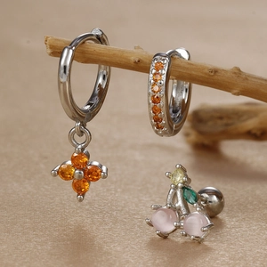 Detail of luxury clover zircon earrings and cherry stud set on a wooden display stand