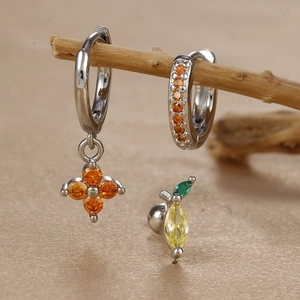 Macro view of clover zircon earrings and lemon studs on a textured satin background