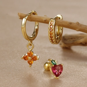 Detailed close-up of lucky clover earrings and apple stud set on a natural wooden branch