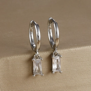 Macro detail of square-cut zircon earrings with polished silver finish on a gold stand