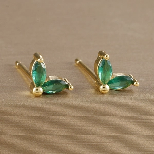 Close-up of golden leaf earrings with marquise-cut green zircons in a vintage luxury style