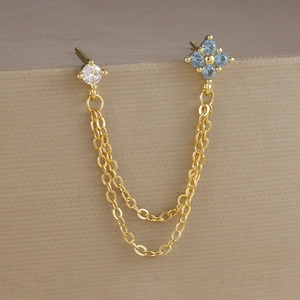 Dettaglio macro di orecchini placcati oro con zirconi blu e catene pendenti