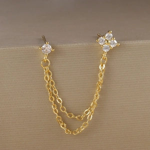 Dettaglio di orecchini a catena placcati oro con zircone e quadrifoglio su supporto in metallo