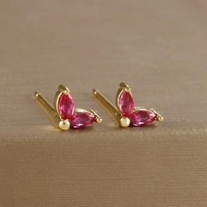 Close-up of gold flower earrings with marquise-cut ruby zircons on a metal surface