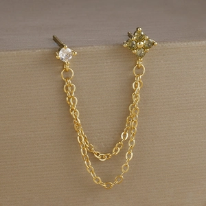 Dettaglio di orecchini a catena dorata con zircone quadrato e gemma verde a fiori