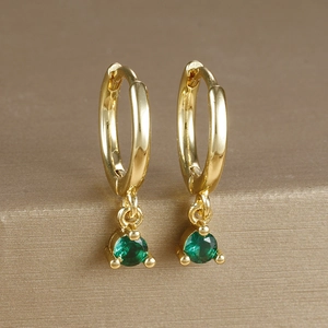 Detailed close-up of gold plated drop earrings with emerald green zircon stones