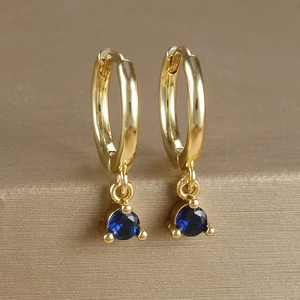 Macro shot of gold-plated hoop earrings featuring a vibrant blue zircon gemstone pendant