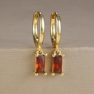 Dettaglio di orecchini placcati oro con nappe di zircone rosso su un supporto testurizzato