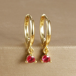 Close-up of gold plated leverback earring with a round red gemstone in 3-prong setting