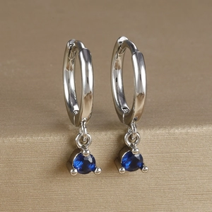 Detailed close-up of silver hoop earrings featuring blue zircon drops in a three-claw setting