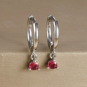 Close-up of silver-tone hoop earrings featuring brilliant-cut red zircon drop pendants