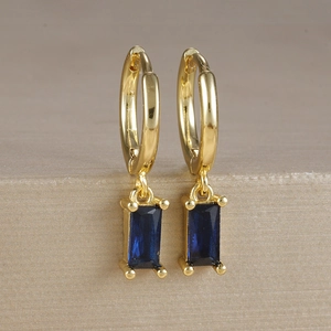 Dettaglio di orecchini placcati in oro con zircone blu quadrato e montatura a quattro griffe