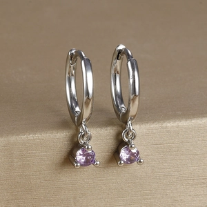 Macro detail of silver-plated hoop earrings featuring claw-set purple zircon drops