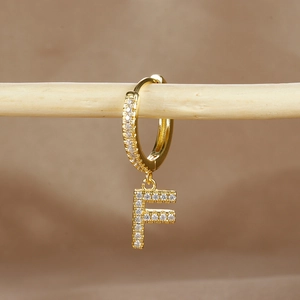 Macro detail of gold-plated earring with letter F pendant and micro-pave zircons