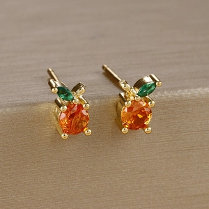 Macro detail of orange-shaped zircon earrings with green leaf stones on gold metal stand