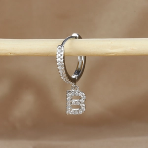 Detailed macro view of silver letter B huggie hoop earring with micro-pave cubic zirconia
