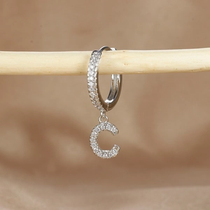 Macro detail of silver hoop earring with crystal pavé letter C pendant on wood support