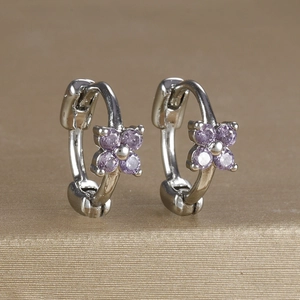 Detailed macro view of silver flower huggie earrings with purple cubic zirconia stones