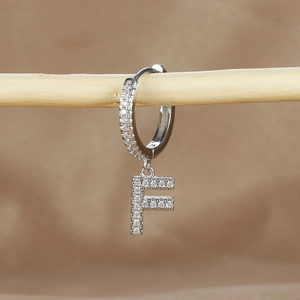 Detail of silver letter F earring with micro-paved zircons on a rustic wooden stand