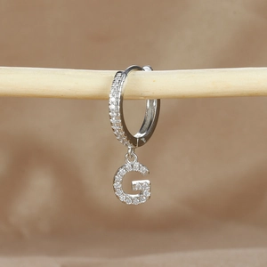 Macro shot of silver letter G hoop earring with micro-paved cubic zirconia stones
