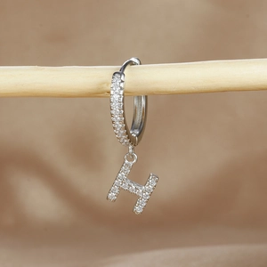 Macro shot of silver letter H earrings with micro-pave cubic zirconia on a wooden stand