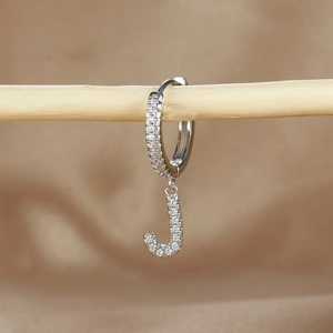 Macro shot of silver letter J hoop earring with cubic zirconia on a wooden branch