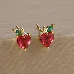 Macro shot of 925 silver needle apple stud earrings with red heart gems and golden base