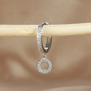 Detailed close-up of micro-paved zircon earrings with silver finish on a wooden branch