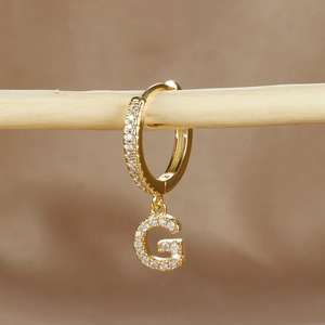 Macro detail of gold-plated hoop earring with G letter pendant and micro-pave zircons