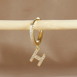 Macro detail of gold-plated earring with letter H pendant and cubic zirconia pavé