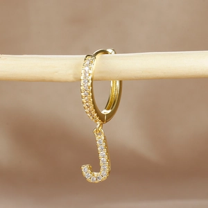 Detail of gold letter J huggie earring featuring pave-set zircon stones on wood stand