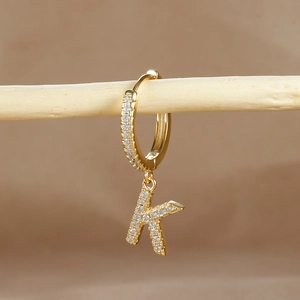 Macro detail of gold-plated earring with sparkling zircon micro-paving on letter K charm