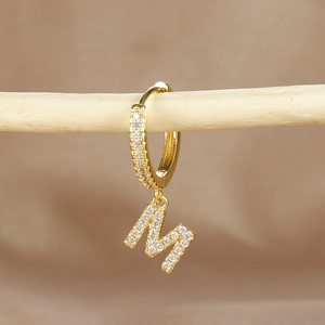 Macro detail of gold hoop earring with letter M pendant and micro-pave zircons