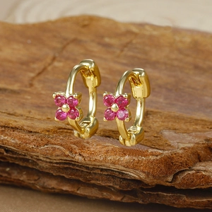 Detail of gold floral huggie earrings with fuchsia zircons on a wooden texture base