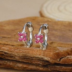 Macro view of silver geometric flower hoop earrings with pink zircons on wood bark