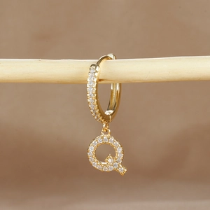 Detail of gold-plated letter Q earring with micro-pave zircons on a wooden stand