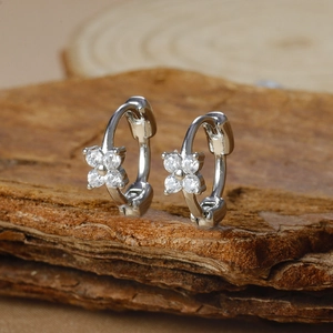 Macro shot of silver flower huggie earrings with four cubic zirconia stones on wood