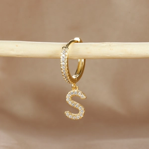 Detailed close-up of gold-plated letter S earring with micro-pave cubic zirconia on wood