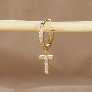 Macro detail of gold T letter earring with micro-paved cubic zirconia on a wooden display