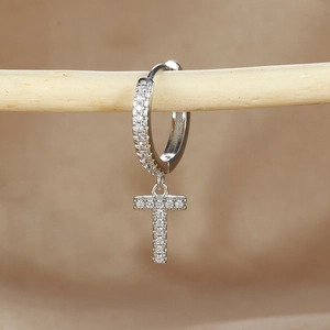 Macro detail of silver letter T drop earring with micro-pave zircons on a wooden branch