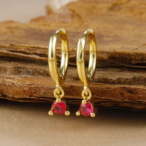 Detailed macro view of gold huggie hoop earrings featuring a round red zircon pendant
