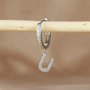 Detailed macro view of silver hoop earring with letter U pendant and micro zircon inlay