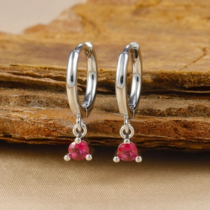Macro shot of silver hoop earrings with vibrant red ruby gemstones in 3-prong settings