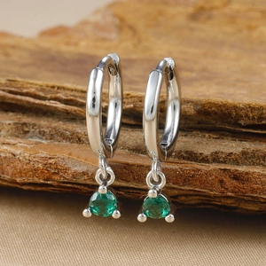 Macro shot of silver-plated hoop earrings with round green zircon charms on textured wood