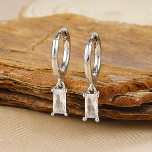 Macro shot of silver geometric earrings with rectangular zircons on dark wood background
